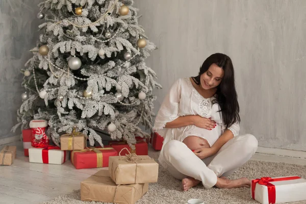 A pregnant woman sitting in the room with the Christmas tree — Stock Photo, Image