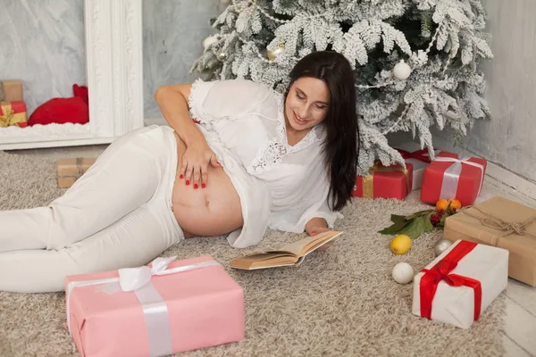 A pregnant woman lies on Christmas Eve Christmas tree with Christmas gifts — Stock Photo, Image