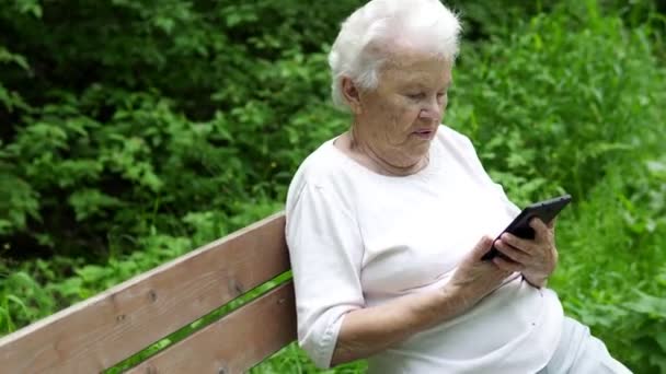 Vieja abuelita mira en el teléfono inteligente Internet — Vídeos de Stock