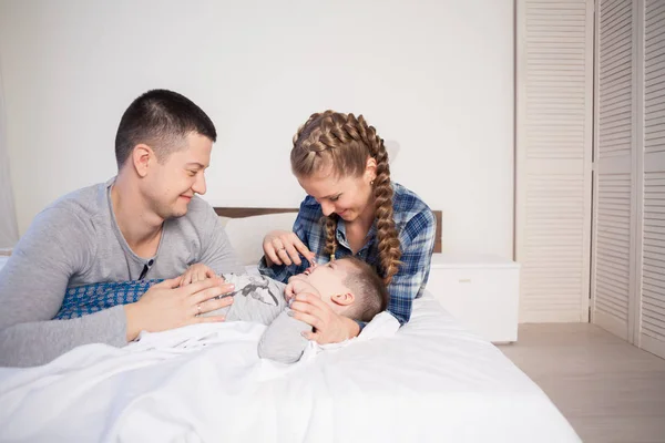 mom dad and son in the morning lying on the bed at home in the morning play