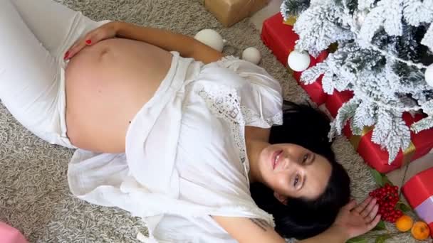 Вагітна мама лежить на ялинці з різдвяними подарунками — стокове відео