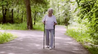 Büyükanne Nordic walking için sopa ile parkta yürüyor