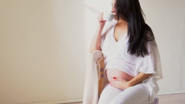 Una donna incinta con una tazza di tè guarda fuori dalla finestra — Video Stock