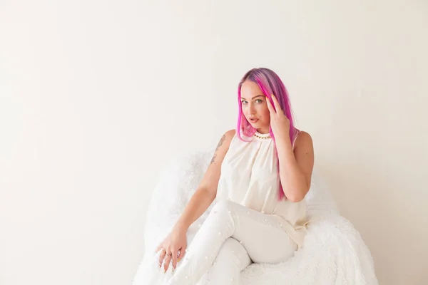 Beautiful woman with pink hair sits in a white armchair — Stock Photo, Image