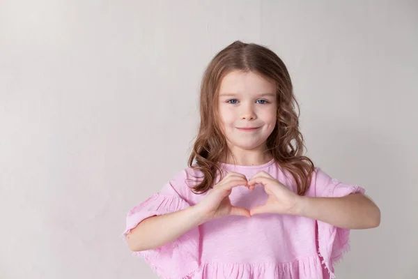 Dziewczynka w różowej sukience pokazuje ręce serce — Zdjęcie stockowe