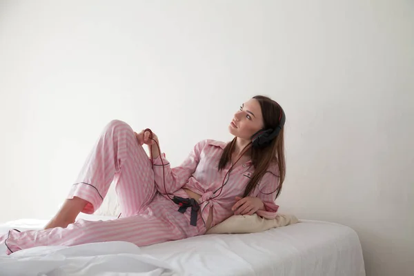 Vrouw in roze pyjama luistert naar muziek met koptelefoon — Stockfoto