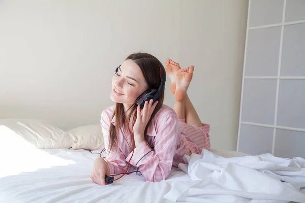 Vrouw in roze pyjama luistert naar muziek met koptelefoon — Stockfoto
