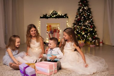 Küçük oğlan ve üç kız Noel hediyelerini açar. Yılbaşı Noel ağacı.