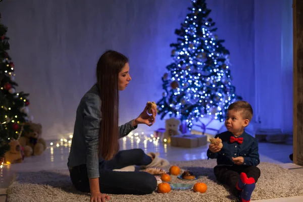 Мать и сын празднуют Новый год у елки с подарками огни Гарланд — стоковое фото