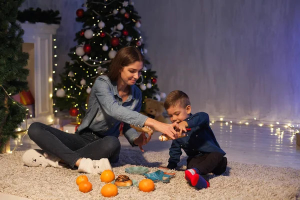 Мать и сын празднуют Новый год у елки с подарками огни Гарланд — стоковое фото