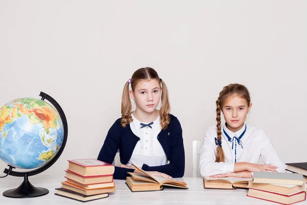 Две девочки в классе Учить учебники у нее на столе глобус — стоковое фото
