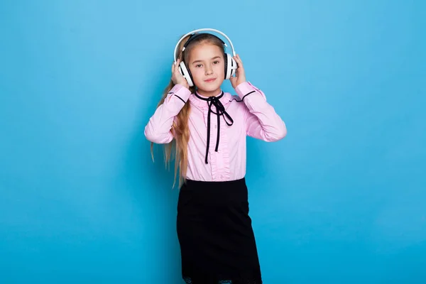 Ritratto di una bella ragazza con le cuffie che ascolta musica su sfondo blu — Foto Stock