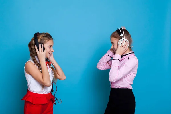 Due belle ragazze con le cuffie che ascoltano musica su sfondo blu — Foto Stock