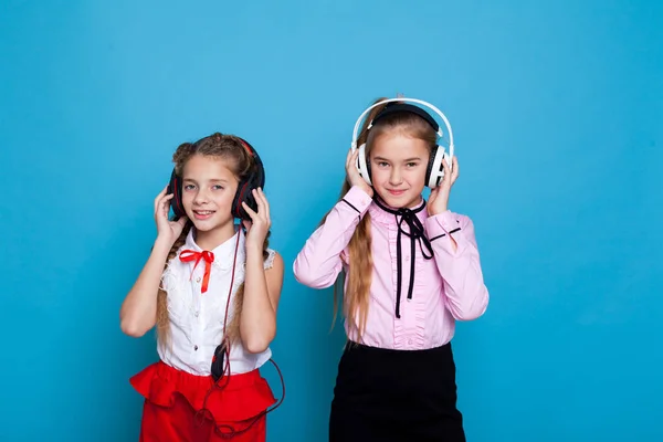 Due belle ragazze con le cuffie che ascoltano musica su sfondo blu — Foto Stock