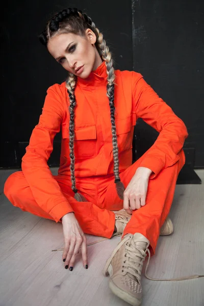 Schöne modische Frau mit Zöpfen in orangefarbenen Overalls — Stockfoto