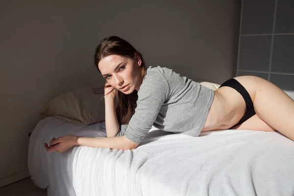 Bela mulher em roupa interior encontra-se na cama no quarto — Fotografia de Stock