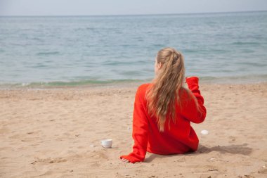 ıssız bir kumlu plajda denize bakarak bir kadın oturur