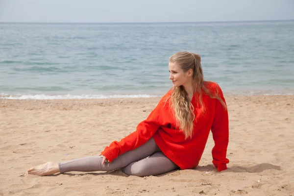 Жінка сидить на покинутому піщаному пляжі, дивлячись на море — стокове фото