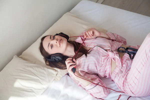 Mooie vrouw in pyjama luisteren naar muziek met koptelefoon in bed slaapkamers — Stockfoto