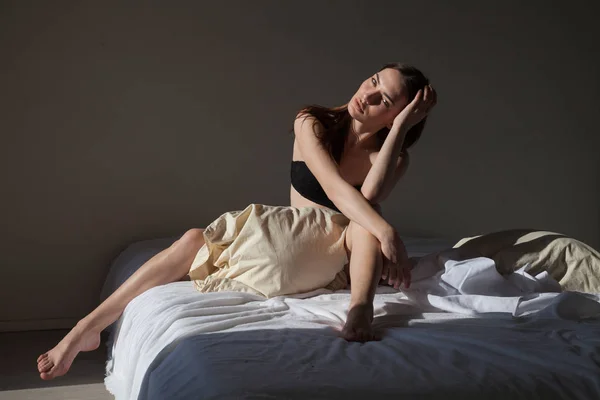 Mooie vrouw in ondergoed zittend op een bed met een kussen slaapkamer — Stockfoto