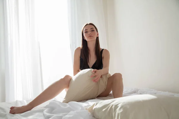 Mooie vrouw in ondergoed zittend op een bed met een kussen slaapkamer — Stockfoto