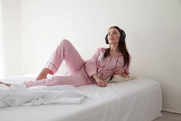 Hermosa mujer en pijama escuchando música con auriculares en dormitorios cama — Foto de Stock