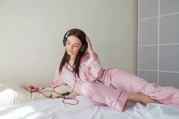ベッド寝室でヘッドフォンで音楽を聴くパジャマで美しい女性 — ストック写真