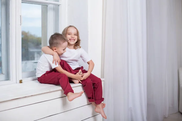 Boy and girl sitting on the windowsill looking out the window — Stock Photo, Image