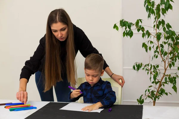 Учительница учит маленького мальчика рисовать за столом — стоковое фото