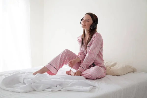 Vrouw in roze pyjama's, luisteren naar muziek in hoofdtelefoons dansen op het bed — Stockfoto