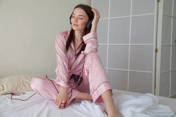 Mulher em rosa Pajamas ouvir música em fones de ouvido dançando na cama — Fotografia de Stock