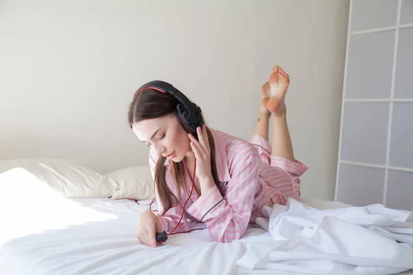 Frau im rosafarbenen Schlafanzug hört Musik über Kopfhörer und tanzt auf dem Bett — Stockfoto
