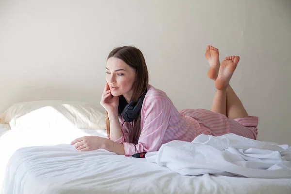 Женщина в розовых пижамах слушает музыку в наушниках, танцующих на кровати — стоковое фото