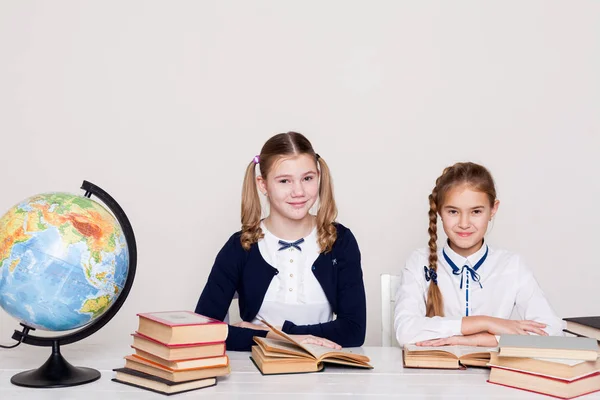 Duas meninas alunas sentadas em sua mesa na lição na escola — Fotografia de Stock