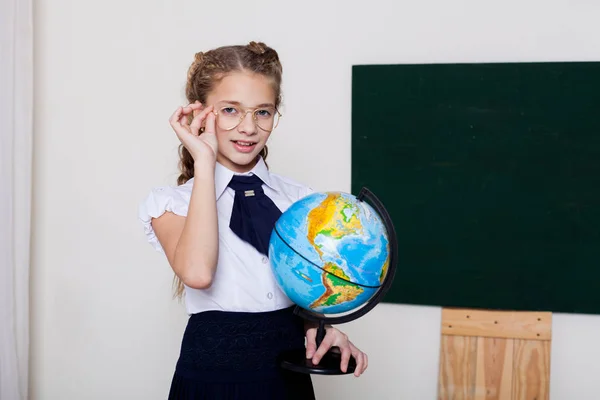 Menina escola menina está de pé no quadro negro com globo — Fotografia de Stock