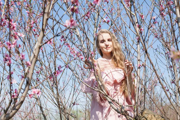 Bela mulher loira em um jardim de pêssego florido na primavera com flores rosa — Fotografia de Stock