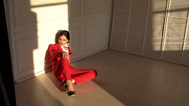 Приваблива брюнетка в червоному костюмі сидить студії — стокове відео
