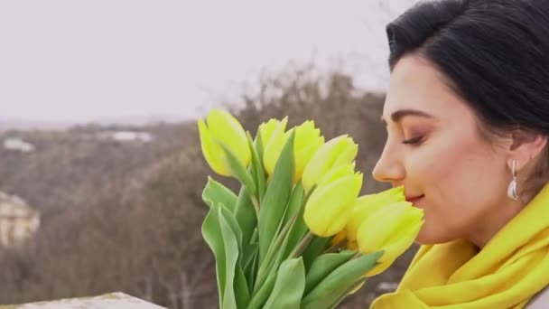 Mujer morena alegre disfrutando del olor de los tulipanes amarillos dado por el hombre amado — Vídeos de Stock