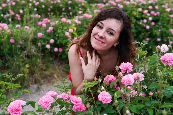 Mulher bonita em vestido vermelho em um campo de rosas florescentes — Fotografia de Stock