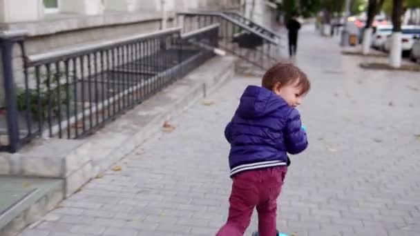 Menino pequeno montando uma scooter na rua — Vídeo de Stock
