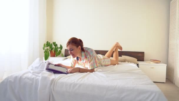 Mujer mira en la tableta acostada en la cama — Vídeo de stock