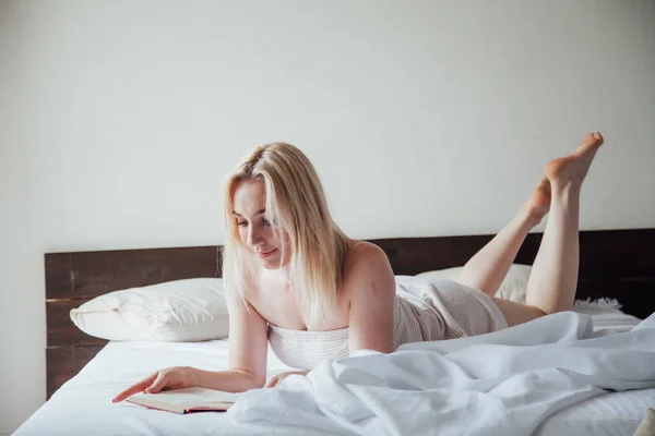 Vrouw blonde leest een boek in de slaapkamer op het bed — Stockfoto