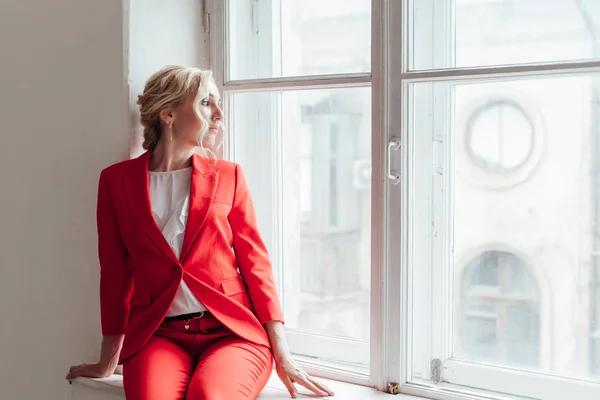 Жінка в червоному діловому костюмі сидить у кімнаті біля вікна — стокове фото