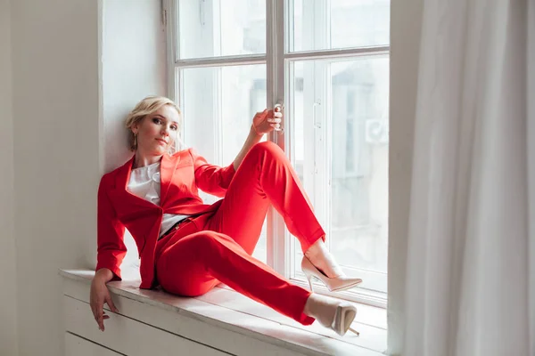 Žena v červeném obleku sedí v pokoji u okna — Stock fotografie