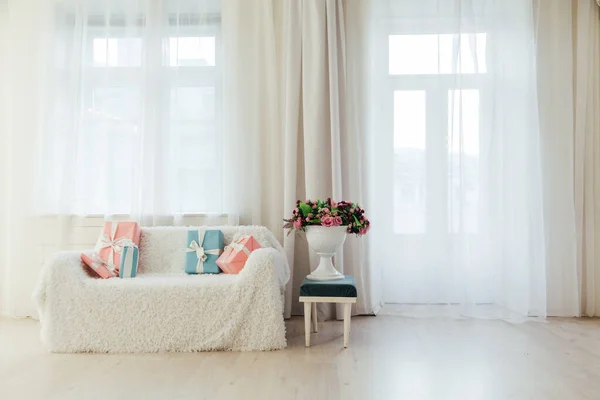 Sofá en el interior de una habitación blanca con regalos de colores y flores — Foto de Stock