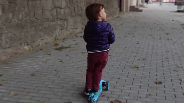 Niño pequeño montando un scooter en la calle — Vídeo de stock