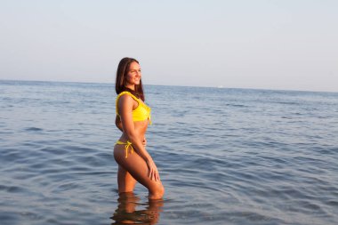 Sarı mayolu güzel, ince kadın okyanusun kıyısında güneşleniyor.