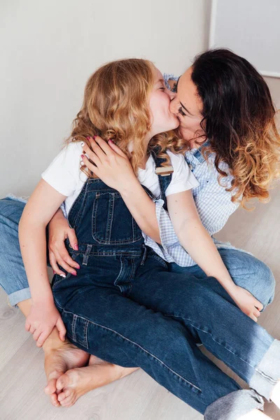 Mom and daughter in jeans sit together cuddling