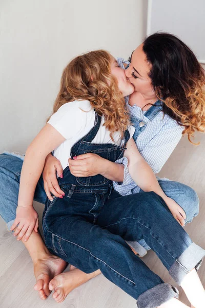 Mom and daughter in jeans sit together cuddling