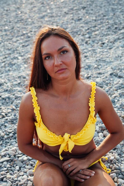 Sárga fürdőruhás barna nő, hosszú hajjal napozik a tengerparton. — Stock Fotó